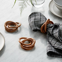 2 wooden napkins rings on a table and 1 napkin ring on a grey plaid napin.