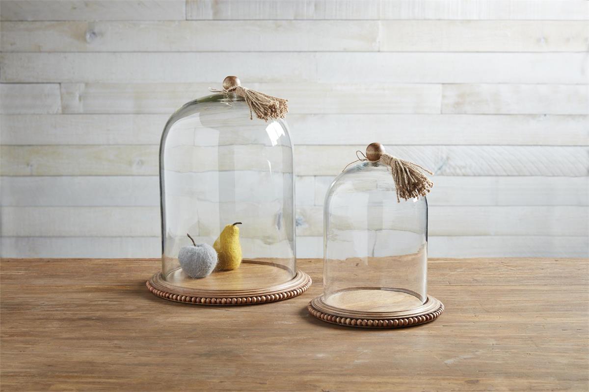 small and large class cloche with tassels displayed on a wooden surface against a white wood slat wall 
