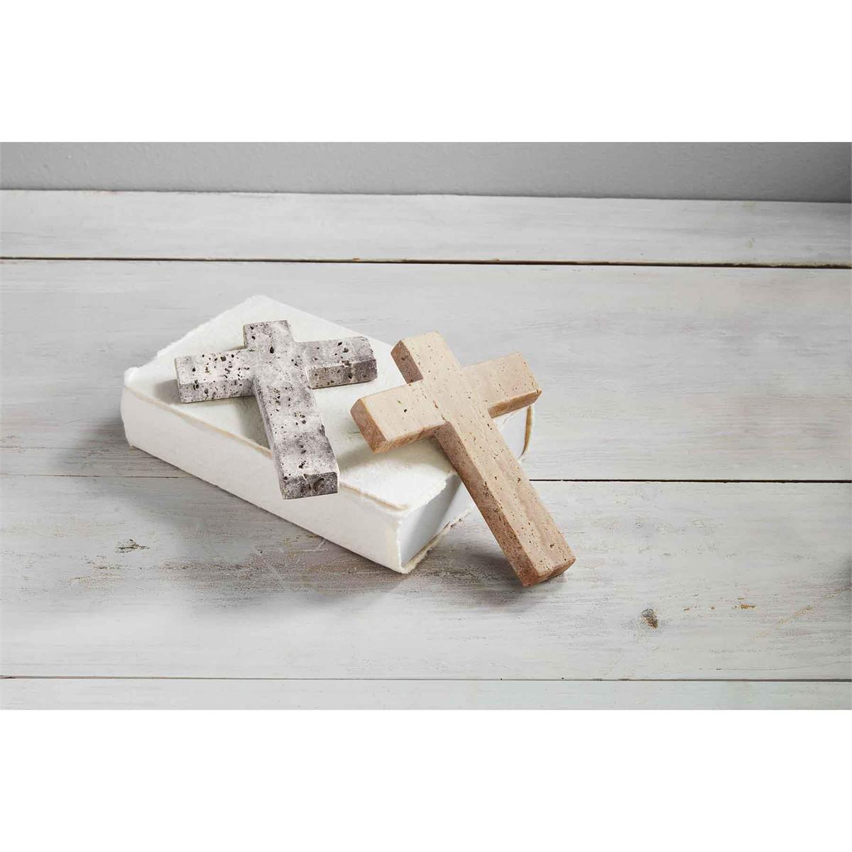 both styles of travertine crosses displayed with a book on a gray wood slat surface