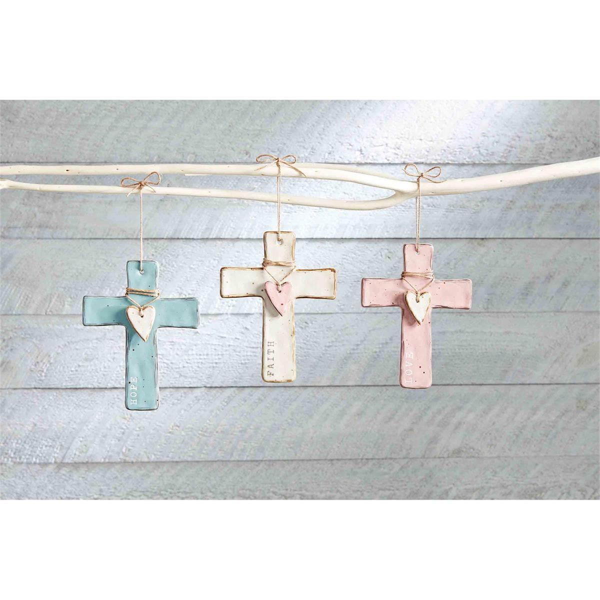 all three colors of heart crosses hanging on a white branch against a whitewashed slat wall