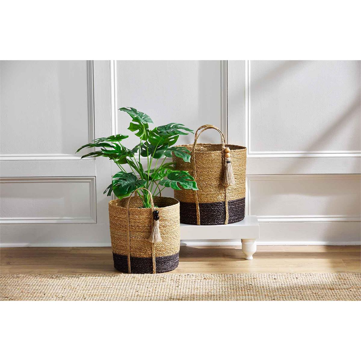 small and large two-toned seagrass baskets displayed on a square riser next to a white wall