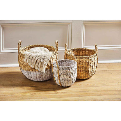 all three sizes of seagrass baskets with handles and one displayed with blankets inside, sitting on a hard wood floor next to the wall