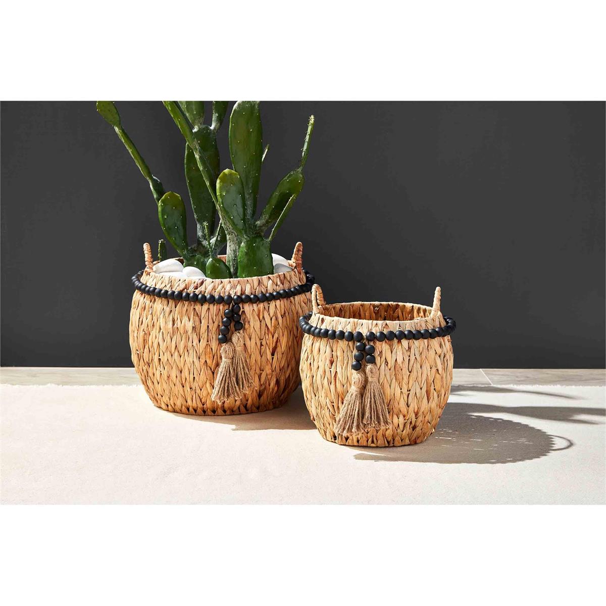 small and large hyacinth beaded tassel baskets, one with a potted cactus on a white floor against a black background