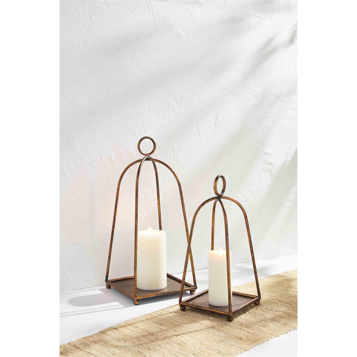 small and large antique brass lanterns displayed with candles inside, sitting on a tan table runner against a white background