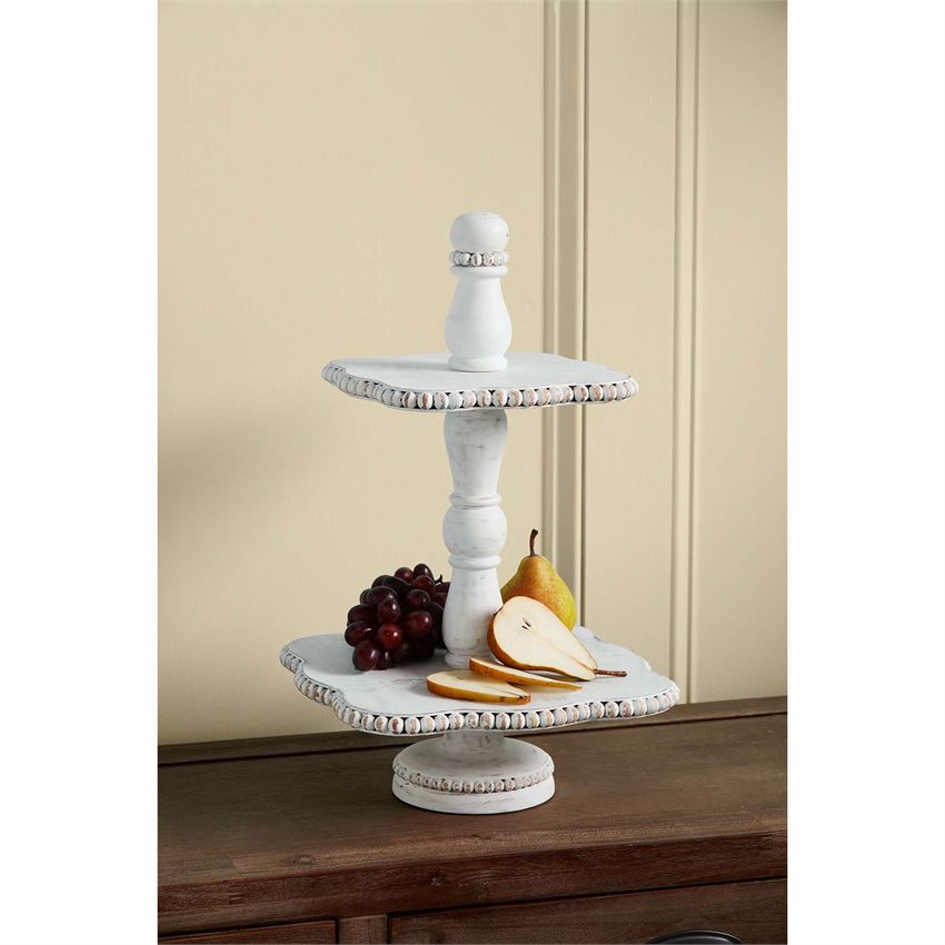 white beaded two tier stand displayed on a dark wood narrow table with pear slices and grapes