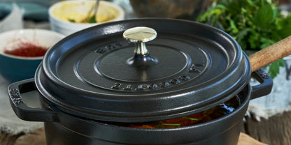 close up of black dutch oven with lid askew showing a glimpse of vegetable stew inside. Various herbs and spices in the background.