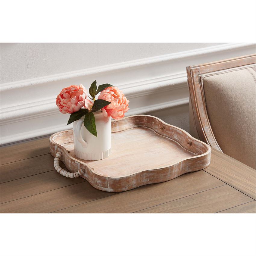 scalloped wooden tray with beaded handles displayed with a pitcher vase filled with pink flowers resting on a side table