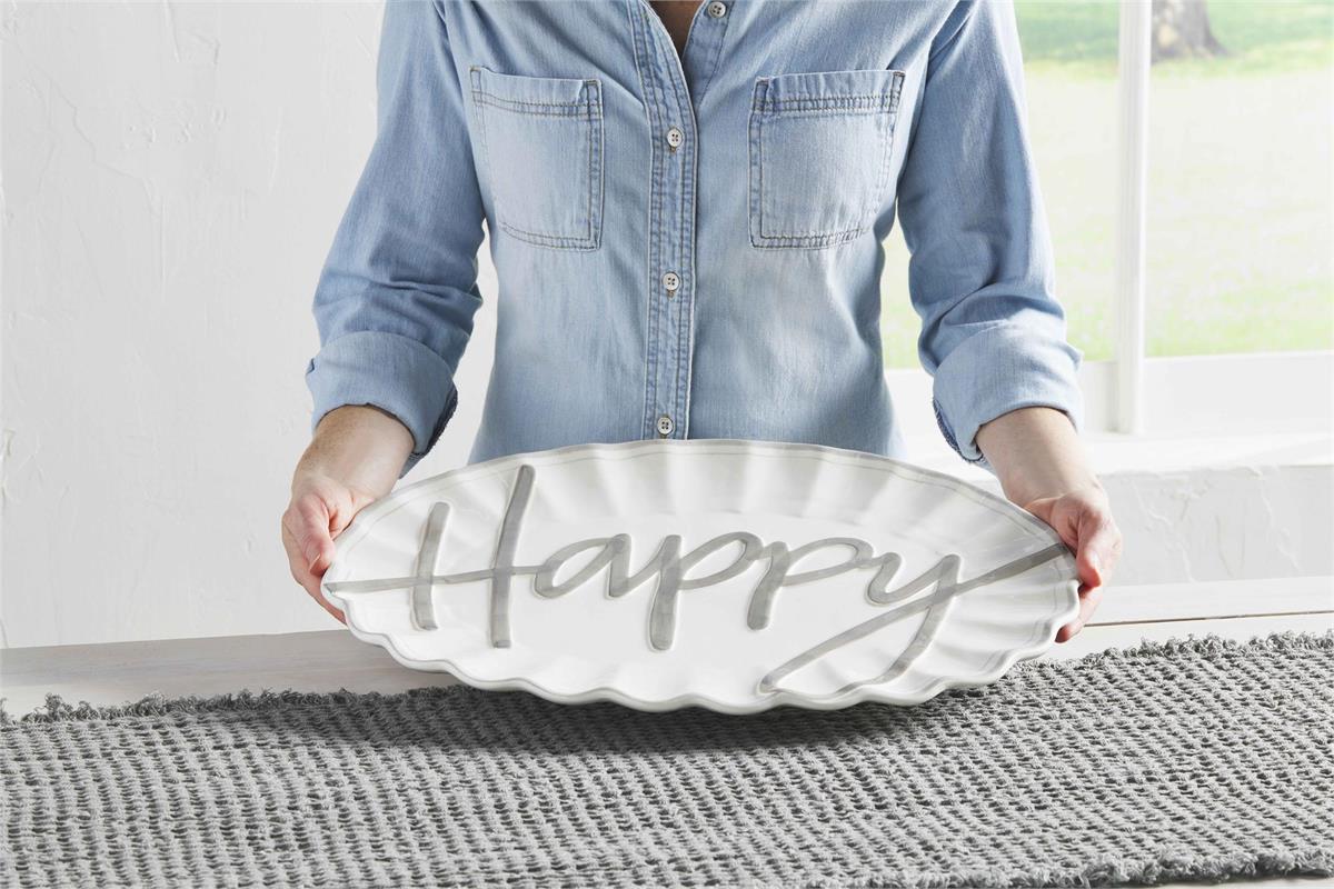 a woman holding the happy serving platter over a white table with a gray table runner