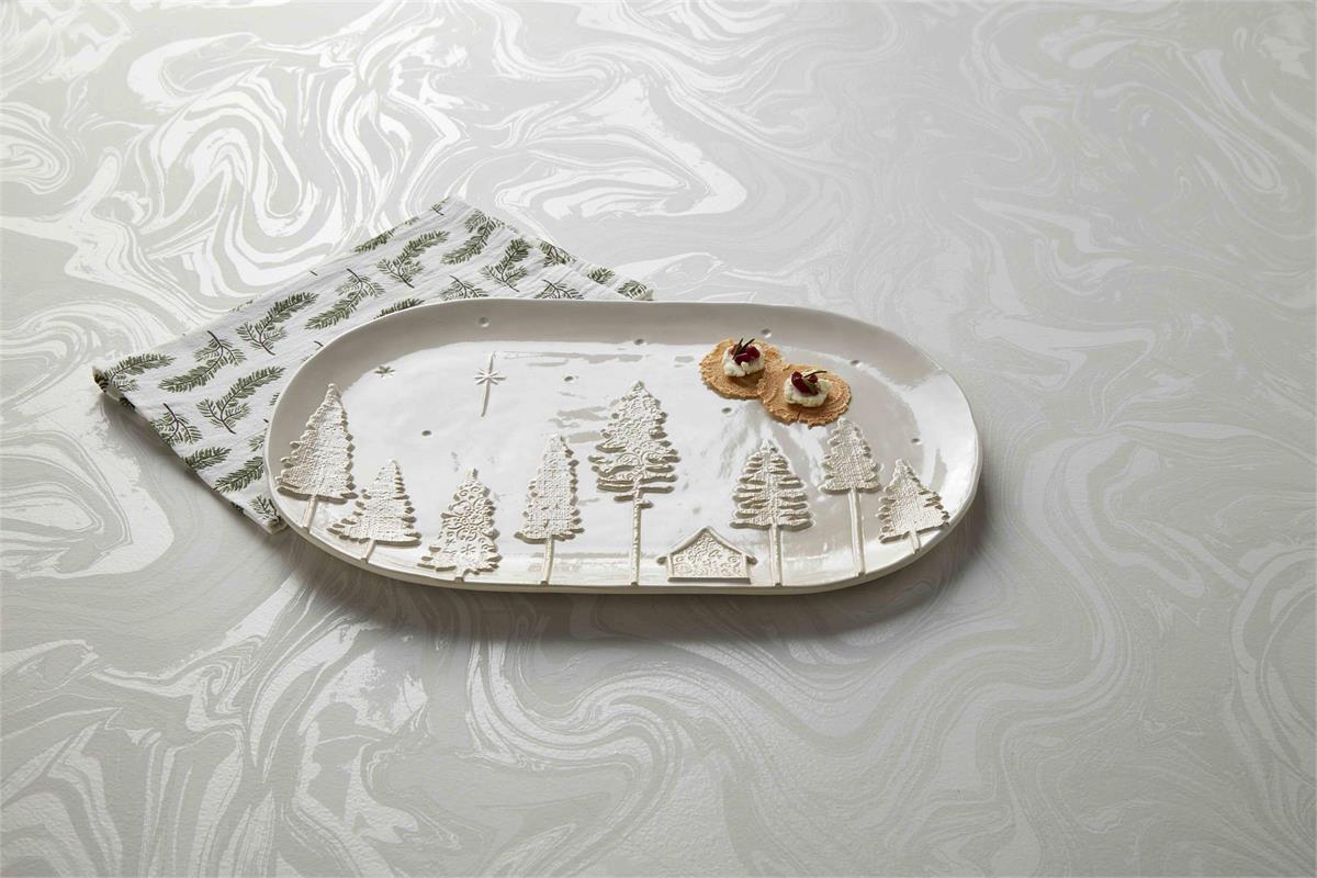 off-white platter with trees and a cabin across the bottom, stars on top, and 2 crackers on it set on a marbled background with a towel.