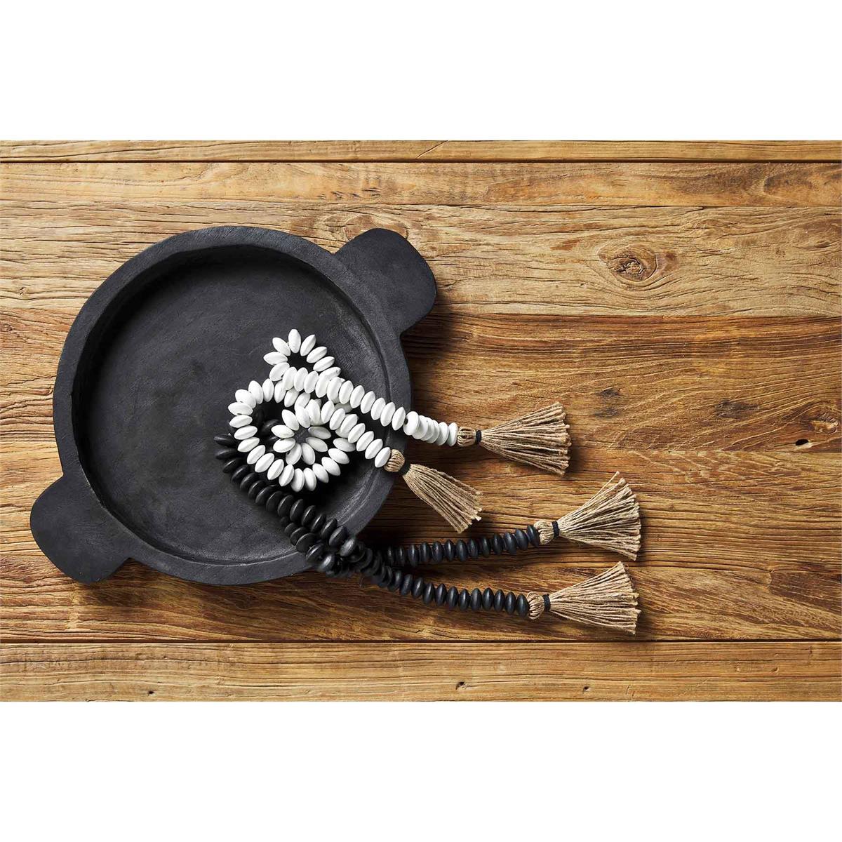one black and one white tassel decor beads displayed in a black tray on a wooden surface
