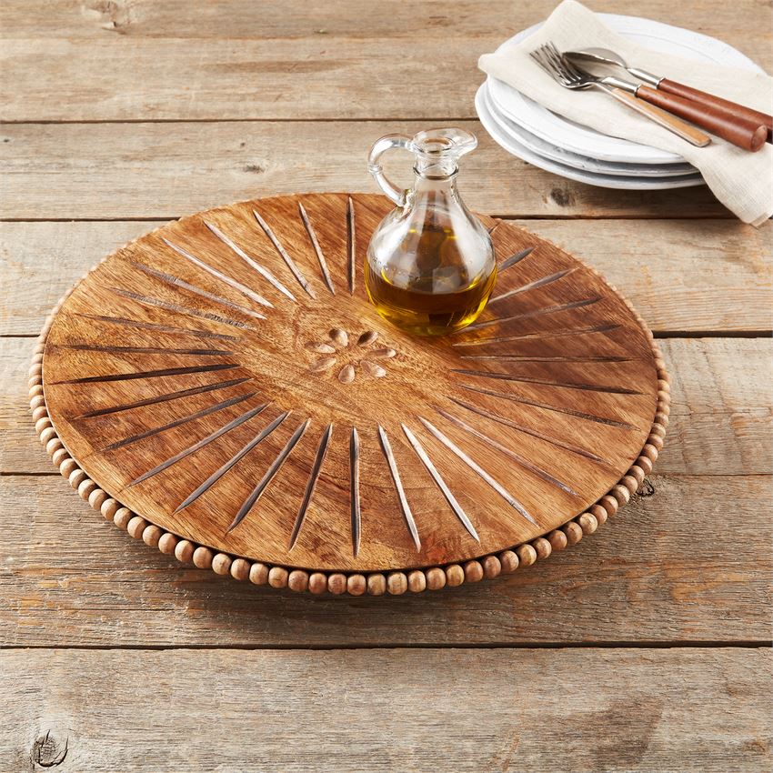 beaded carved wood lazy susan displayed on a rustic wood slat table next to a stack of plates and flatware