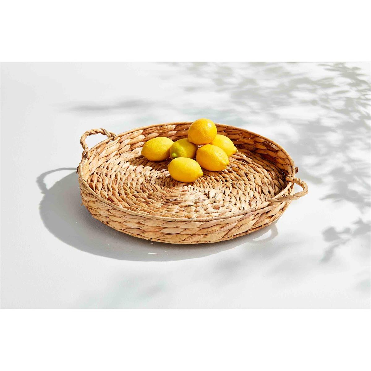 woven lazy susan with handles partially filled with lemons on a white surface outside with shadows of leaves