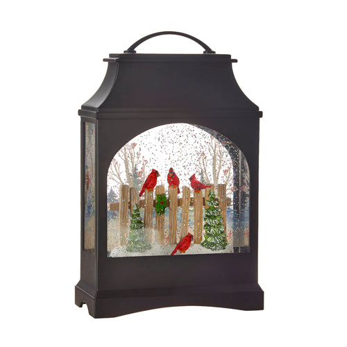 black lantern filled with water, glitter, and cardinals perched on a fence.