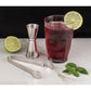 the kitchen ice tongs displayed next to a drink a lime a jigger and mint leaves on a mostly white surface