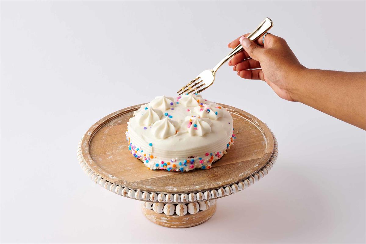 wooden beaded cake stand displayed with a small cake and a persons hand with a fork taking s piece from it