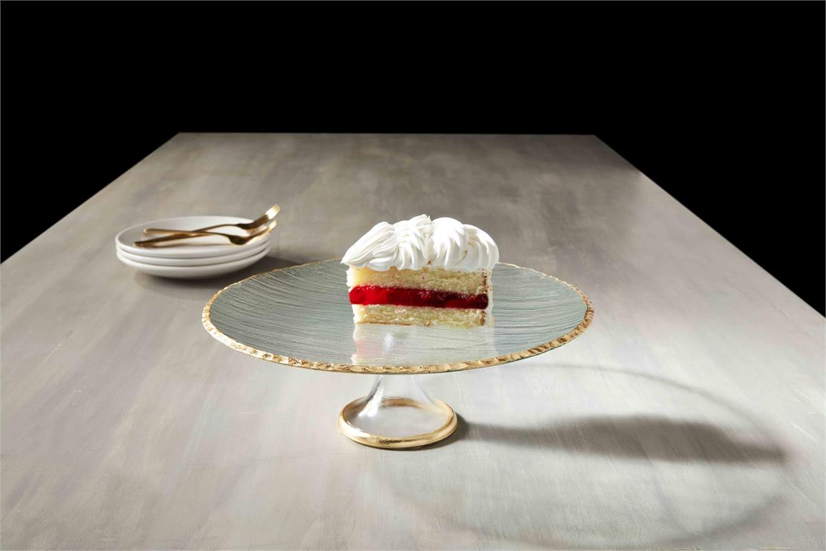 glass cake plate on table with a slice if layer cake on it and a stack of plates and forks on the background.