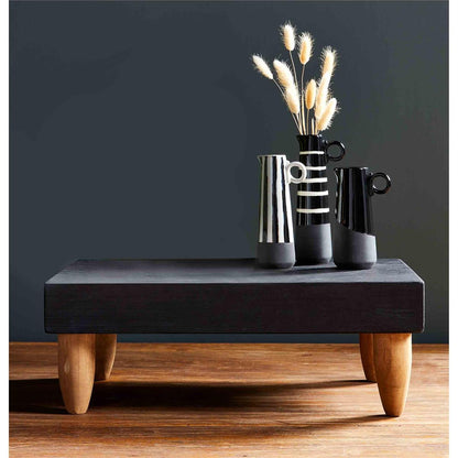 black footed serving board displayed with three sizes of black and white vases on a wooden surface against a black background