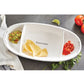 fiesta chip and dip serving set displayed with chips, salsa, guacamole next to herbs, tomatoes, and a towel on a gray surface
