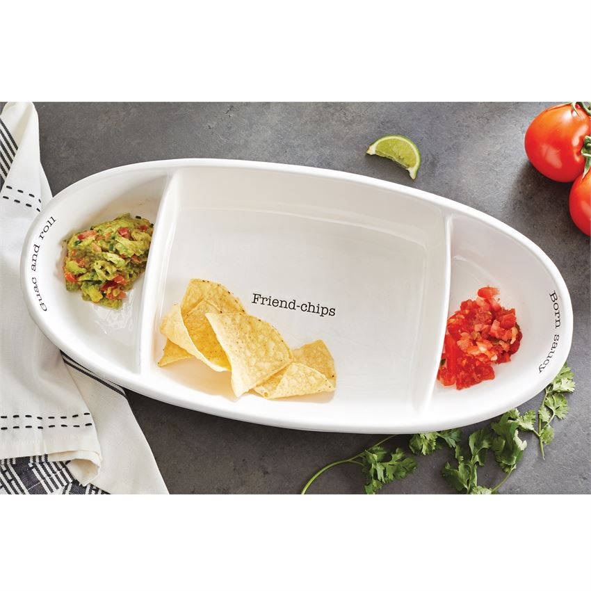fiesta chip and dip serving set displayed with chips, salsa, guacamole next to herbs, tomatoes, and a towel on a gray surface