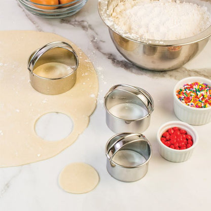 the set of three cookie cutters displayed next to rolled pastry and mixing bowl on a white marble background
