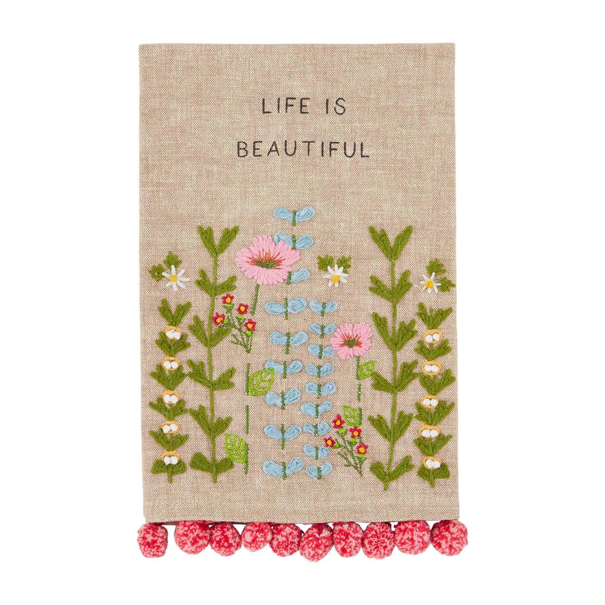 life is beautiful floral embroidered towel is tan with a pink pom trim against a white background