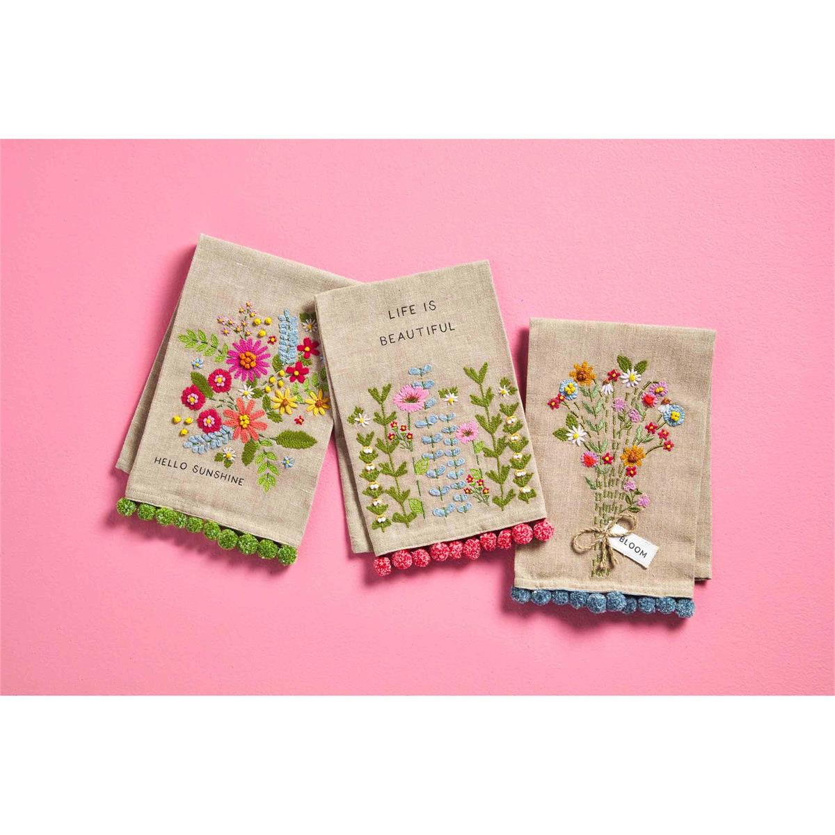 all three styles of floral embroidered pom towel displayed against a pink background