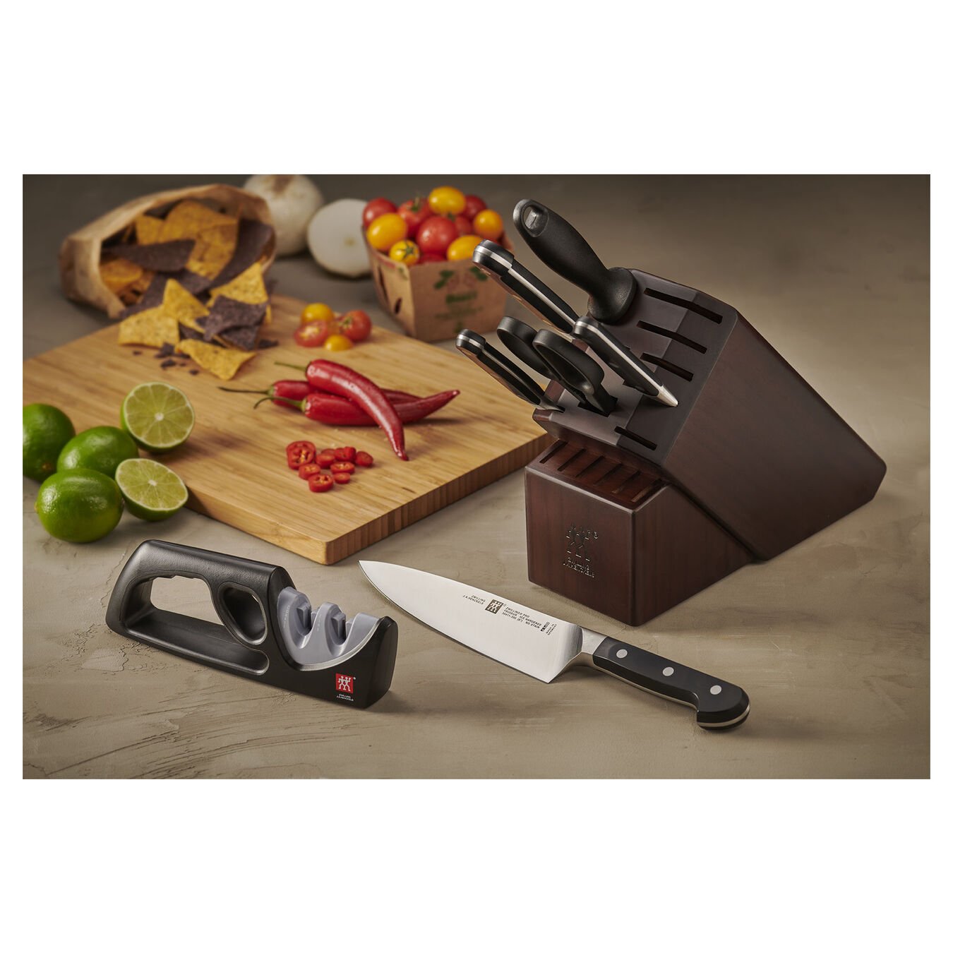 knife block with knives and sharpener  on a marble countertop with cutting board covered with sliced limes, chilies, and tomatoes.