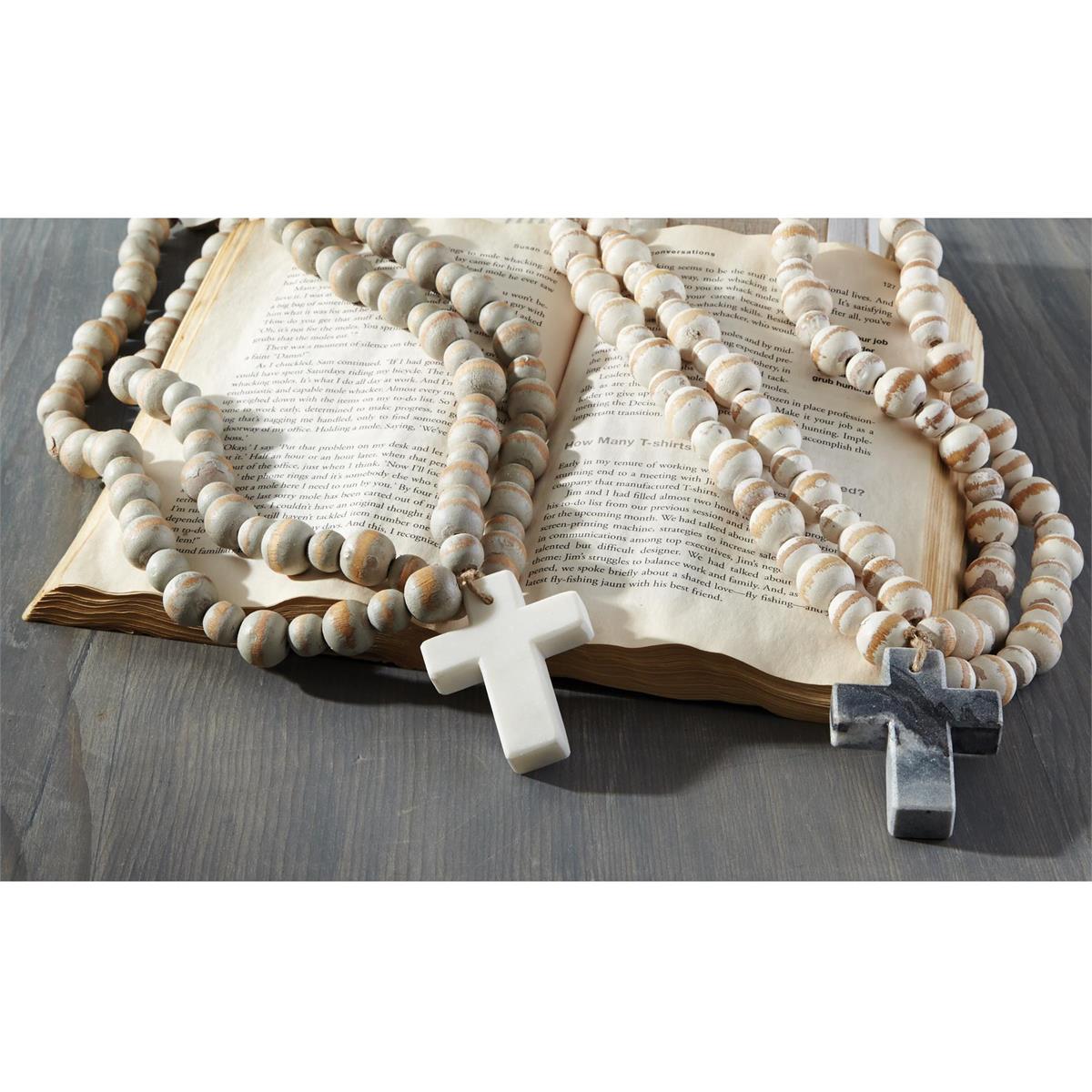 what and marble cross with decorative beads displayed over an open book on a gray table