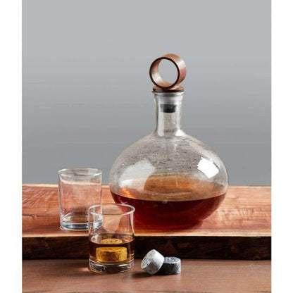 textured glass decanter displayed next to two glasses and whisky rocks on a live edge serving board