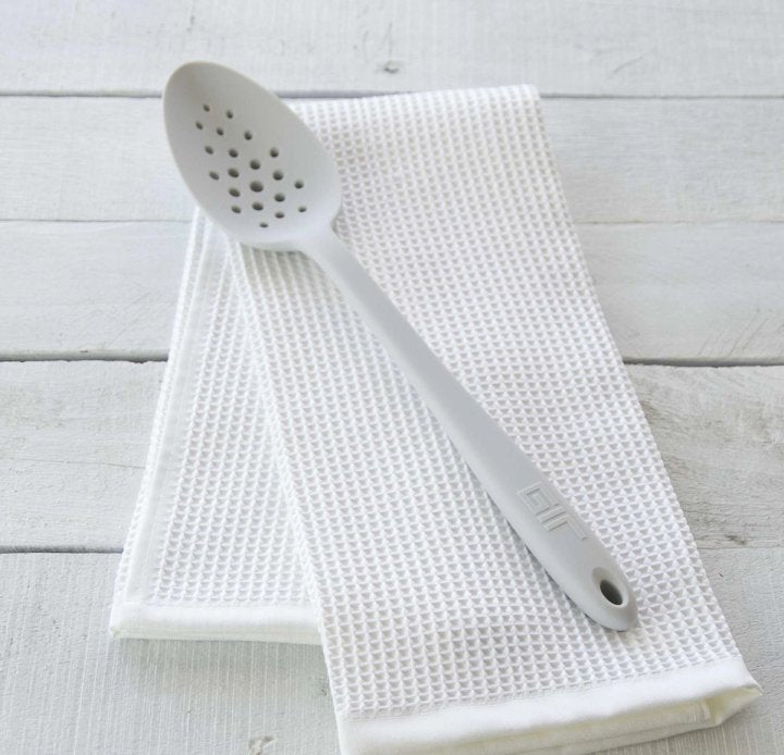 perforated spoon laying on a white dishtowel on a wooden countertop.