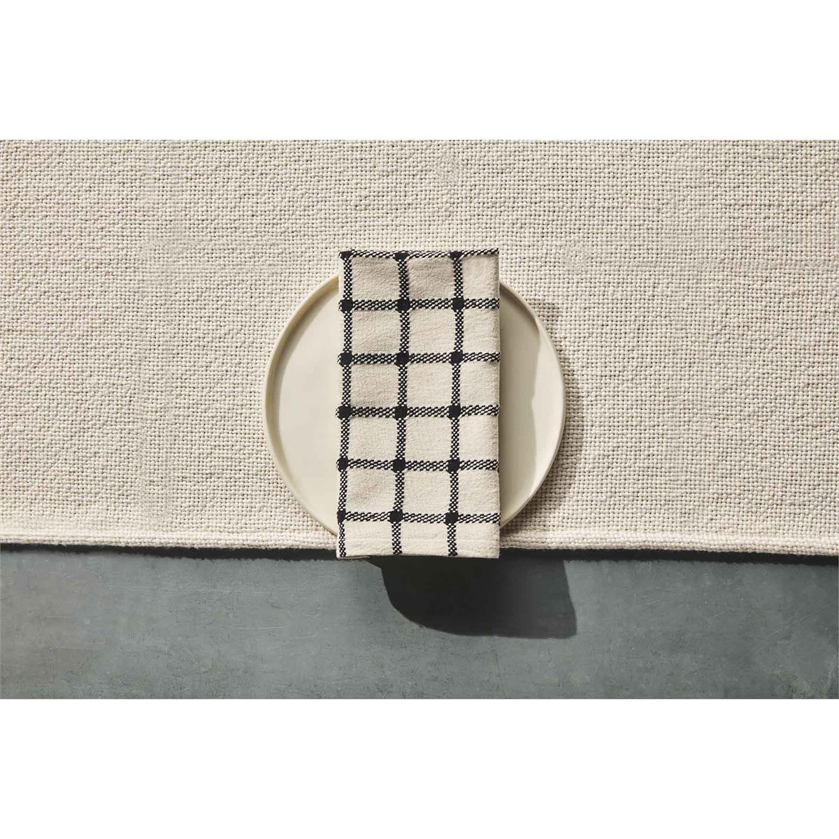 windowpane napkin displayed on a cream plate sitting on a tan table runner