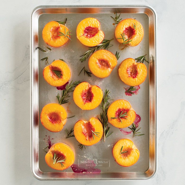 half sheet pan filled with sliced peaches and rosemary sprigs.
