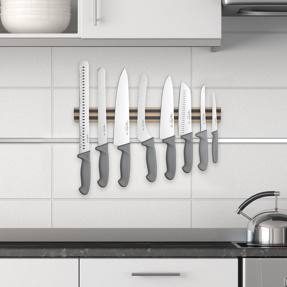 18 inch kitchen magnetic knife holder bar displayed with multiple knives on it and attached to the backsplash in a kitchen next to the stove