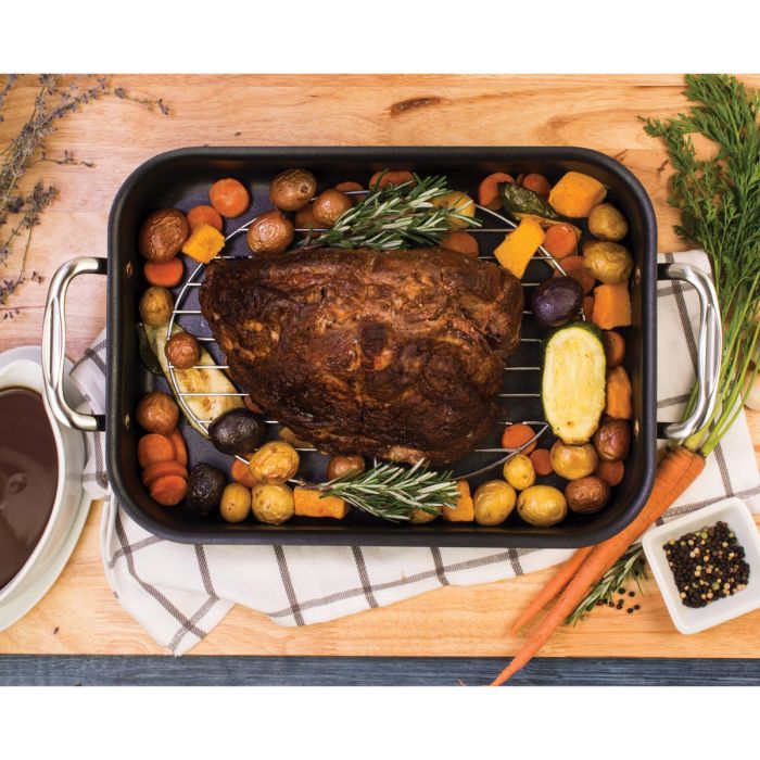 the oval roasting rack displayed in a roasting pot with a roast sitting on a wooden surface surrounded by spices