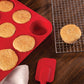 the silicone muffin pan filled with baked muffins displayed next to a cooling rack and spatula on a dark stained wood surface
