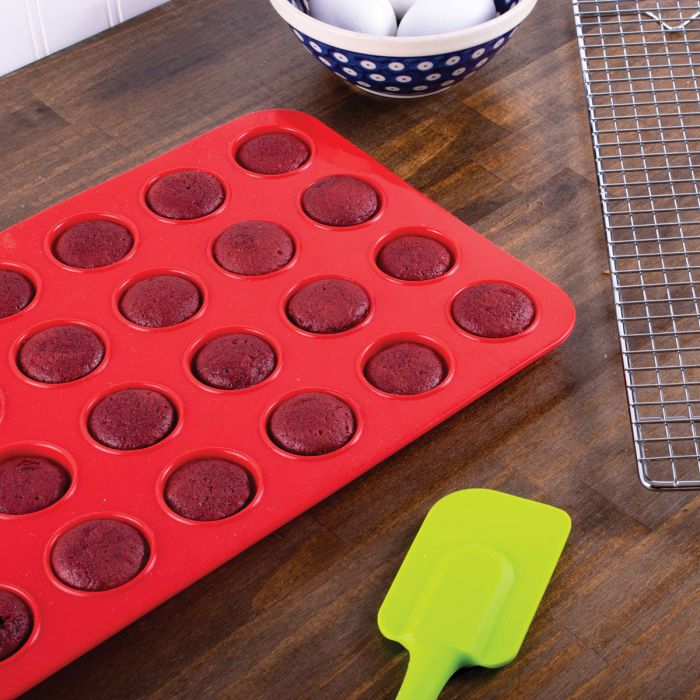 the silicone mini muffin pan displayed on a dark stain wooden surface filled with muffins next to a spatula and cooling rack
