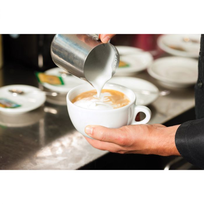 the stainless steel frothing pitcher being used to prepare a cup of espresso in a kitchen