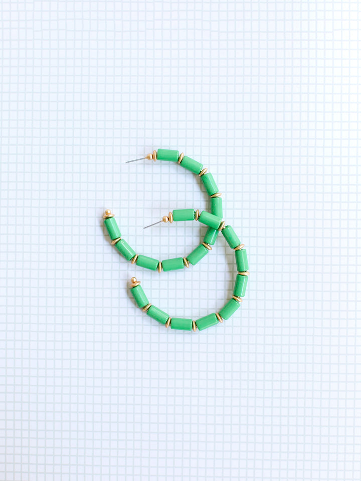 green and gold beaded hoop earrings on grey grid background.