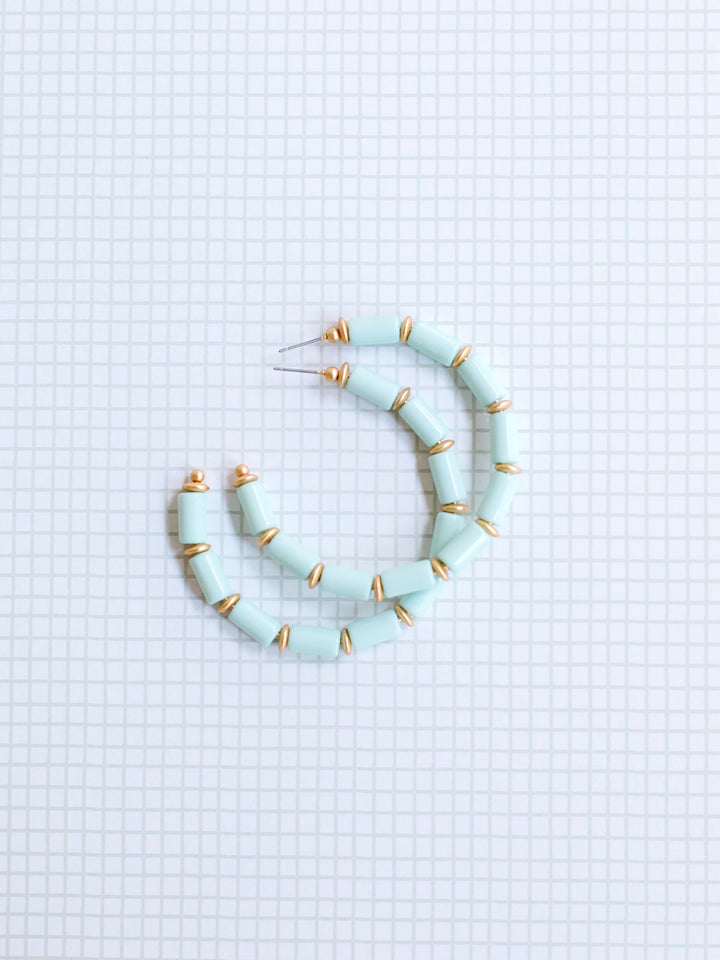 mint and gold beaded hoop earrings on grey grid background.