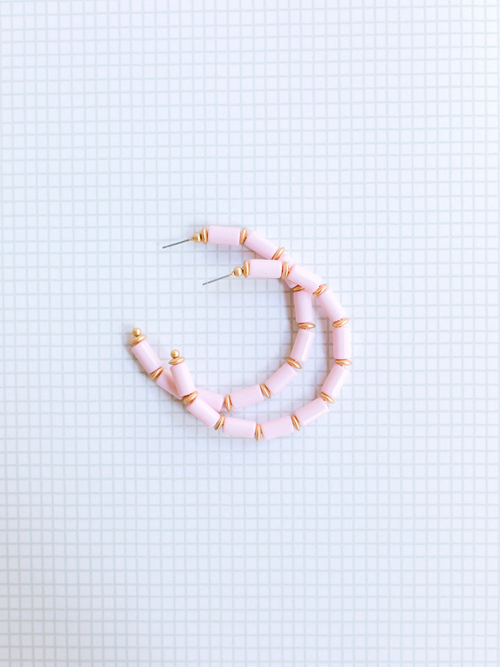 blush and gold beaded hoop earrings on grey grid background.