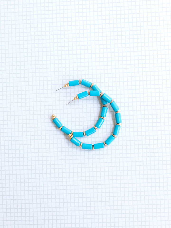 blue and gold beaded hoop earrings on grey grid background.