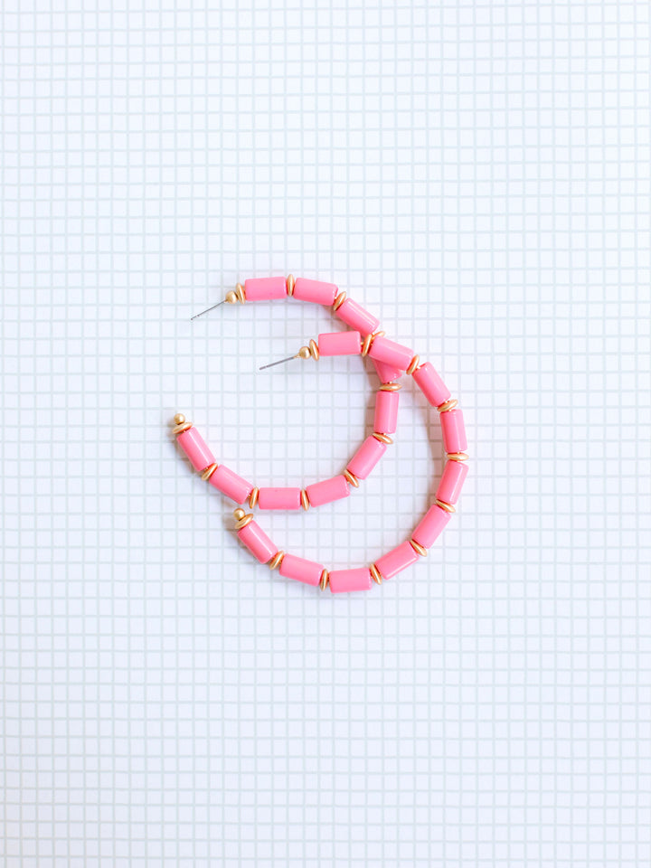 pink and gold beaded hoop earrings on grey grid background.