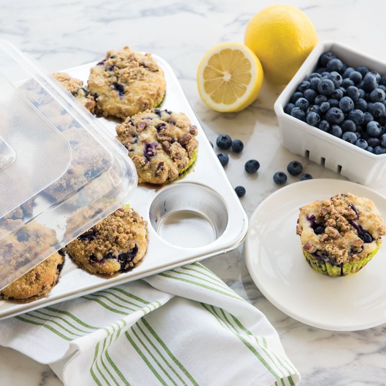 blueberry muffins in pan, one muffin on a plate, and basket of blueberries.