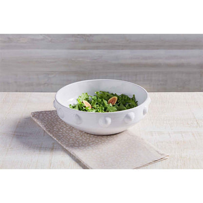 raised dot serving bowl filled with salad and displayed on a folded towel on a white wooden surface