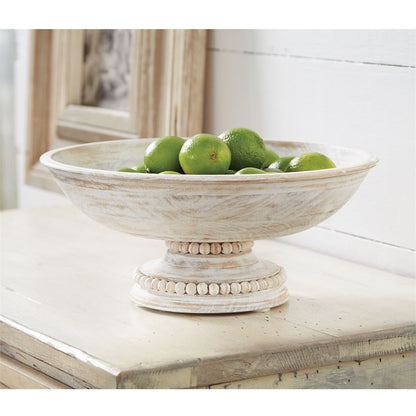 beaded wood pedestal bowl filled with limes displayed on a whitewashed wood surface