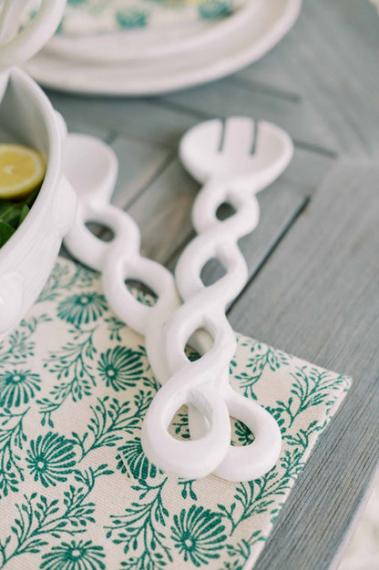 white twisted server set displayed on a table setting next to a bowl of salad on top of a green and white table runner