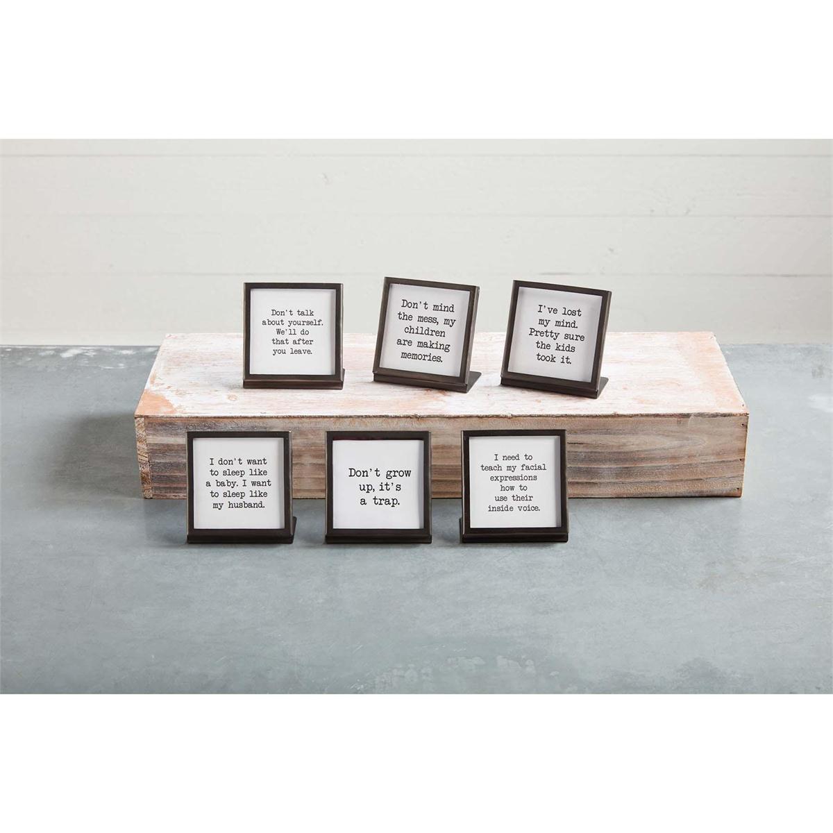 six different black metal framed sayings displayed on a wood board and gray table