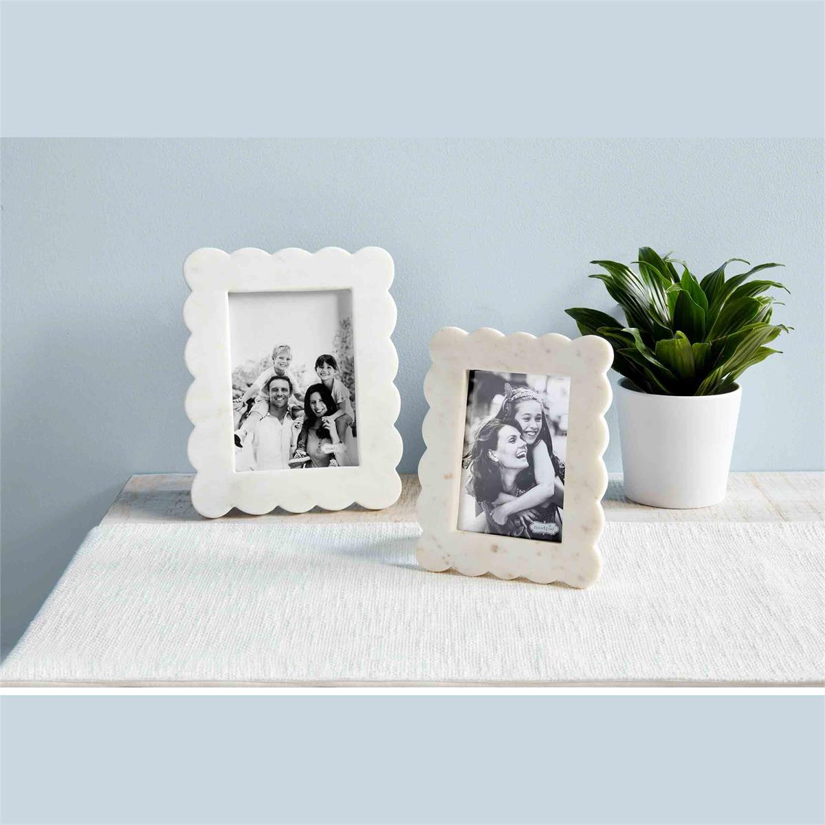 both sizes of scalloped marble frames displayed on a white dresser next to a potted leafy plant