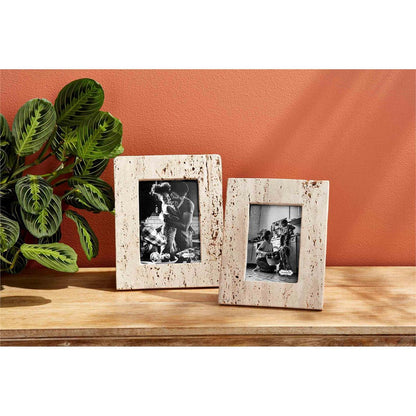 small and large cream travertine frames displayed on a light wood hall table against a coral wall next to a green plant