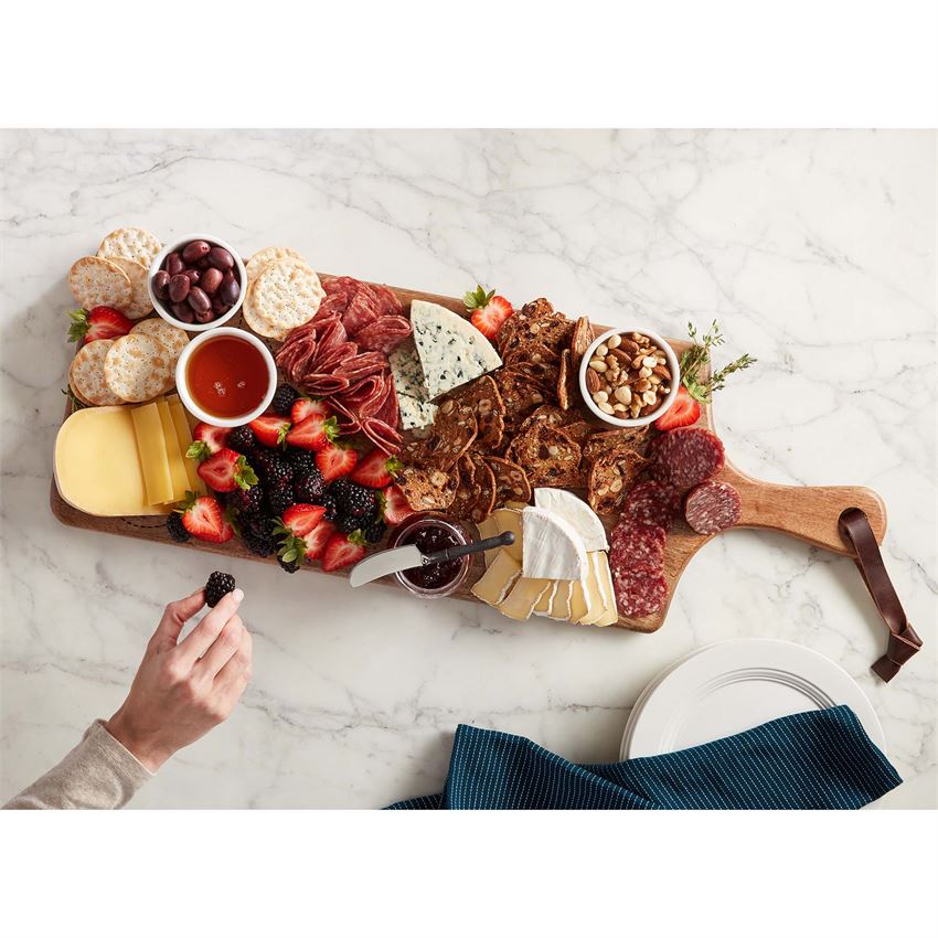 charcuterie serving board displayed with meats cheeses fruits and dips on a white marble countertop